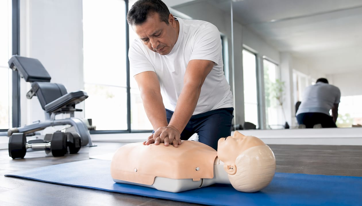 Un hombre practica maniobras de reanimación cardiopulmonar sobre un maniquí durante una clase.