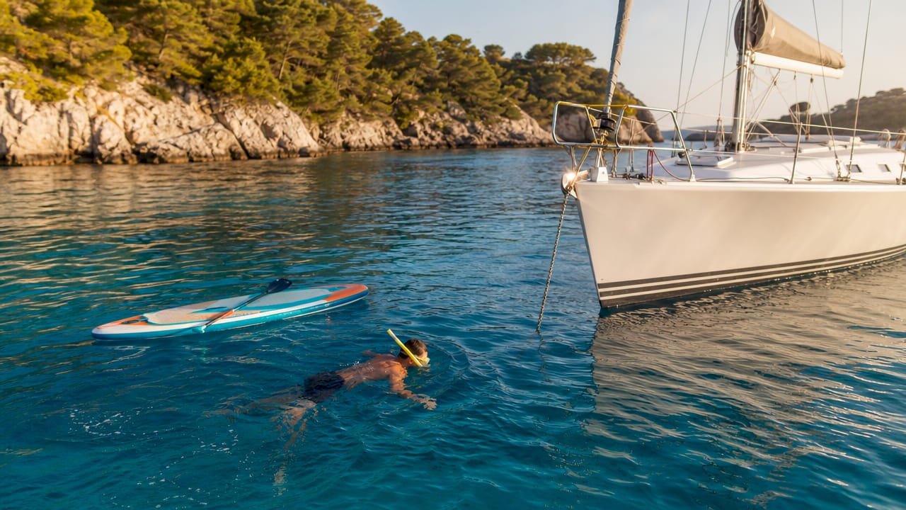 Snorkeler and paddleboard near anchored sailing yacht