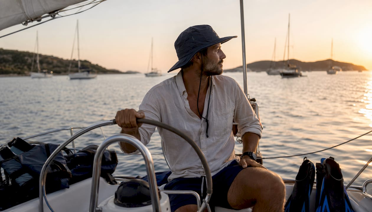 Solo traveler steering sailboat at sea with flotilla nearby