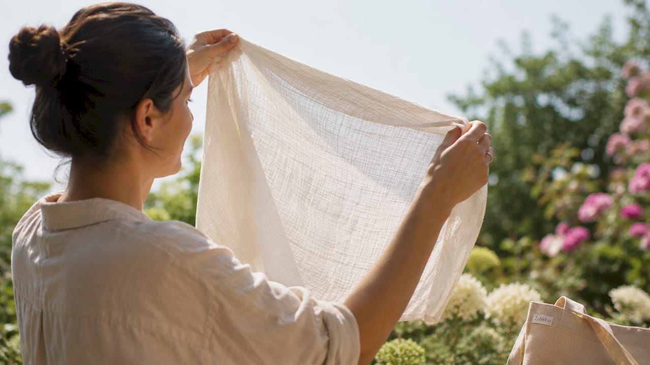 Hands holding muslin fabric to window light for breathability test