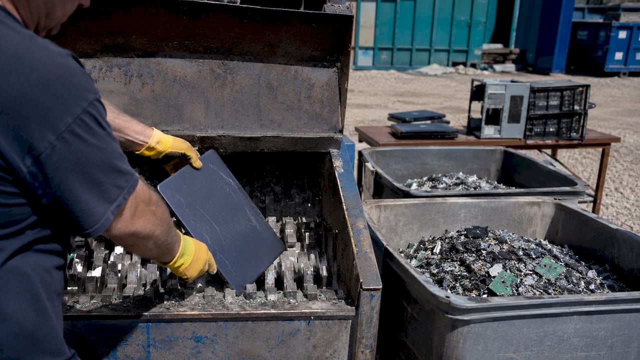 Hands feeding laptop into e-waste shredder machine
