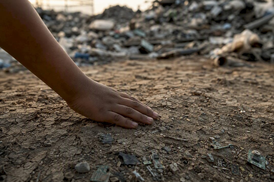 Child's hand near contaminated soil and electronic waste