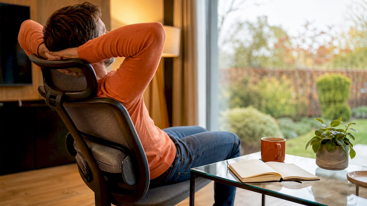 Man zit comfortabel op een ergonomische bureaustoel met lendensteun in zijn thuiswerkplek.