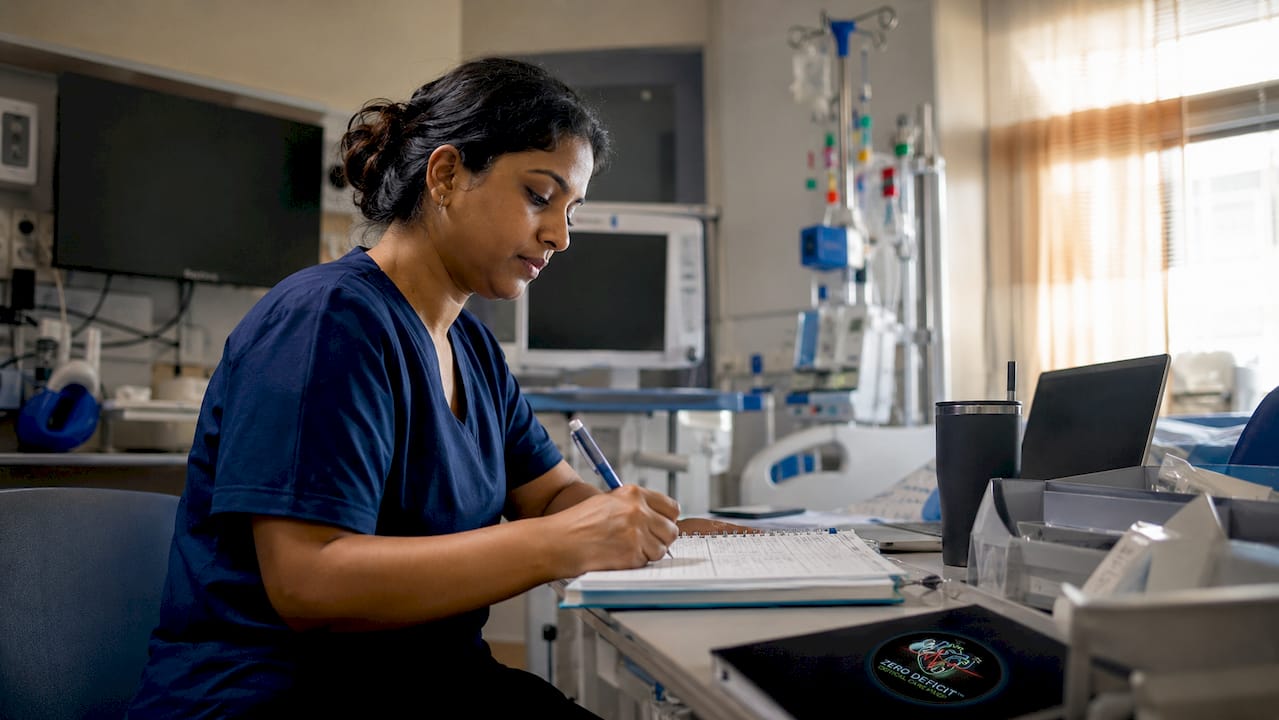 ICU nurse reviewing progress log beside workstation