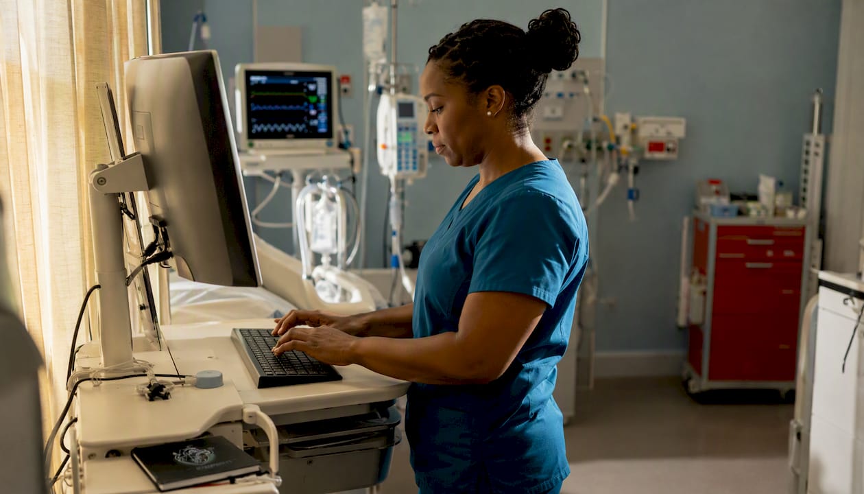 Nurse charting beside ICU patient bed
