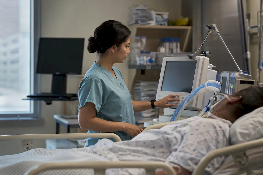 Nurse adjusting ventilator in adult ICU room