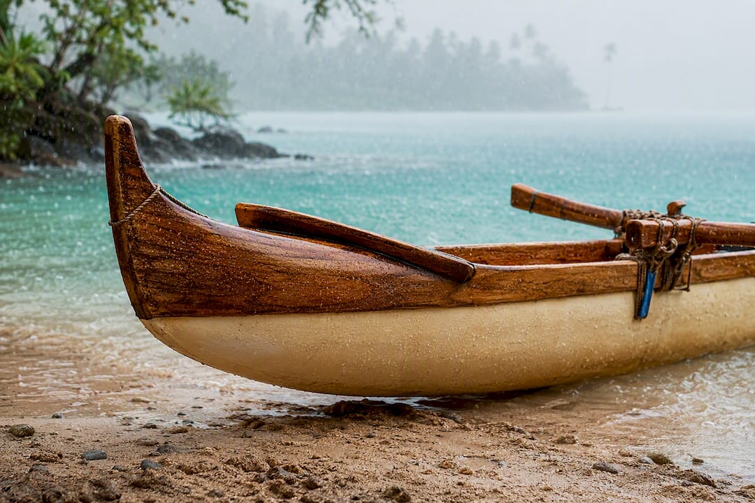 Outrigger canoe beside a rain-softened Hawaiian shoreline