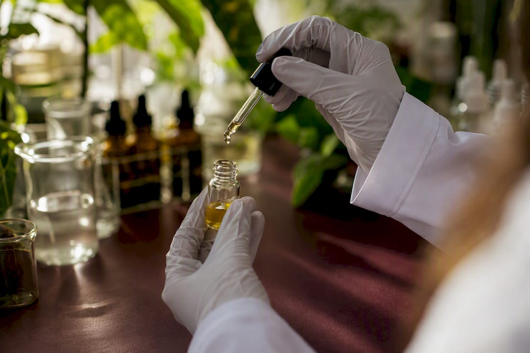 Gloved hand dripping CoQ10 antioxidant oil into vial