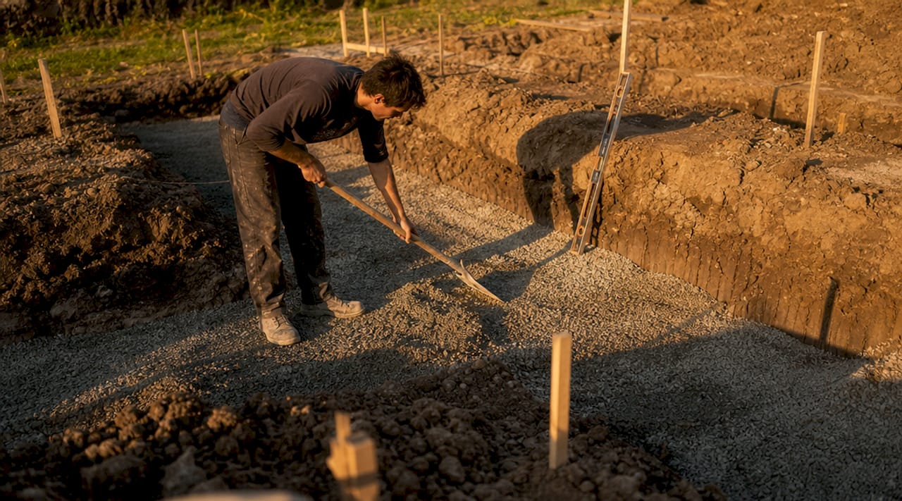 Worker placing gravel in foundation footing trench