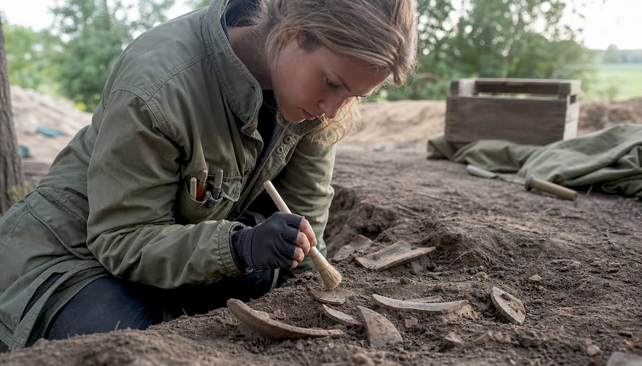 Hands brushing medieval pottery shards in excavation
