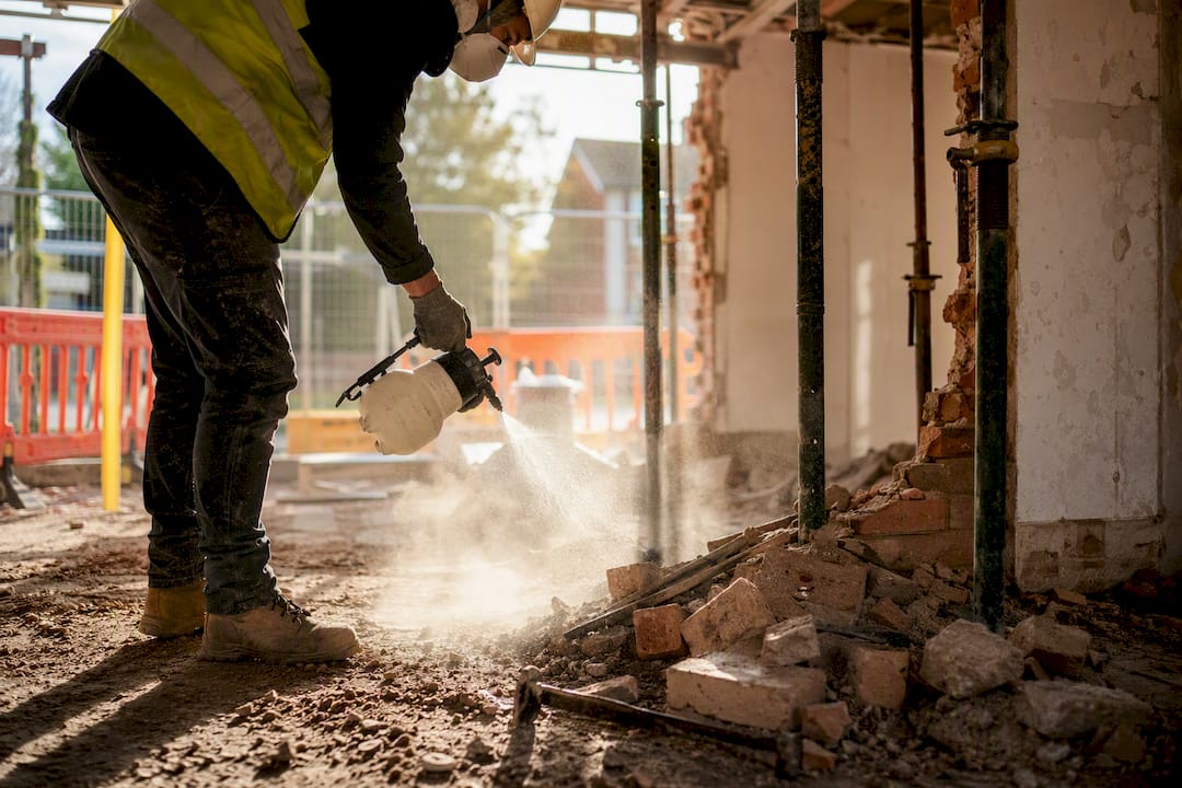 Worker spraying mist to control dust on demolition site