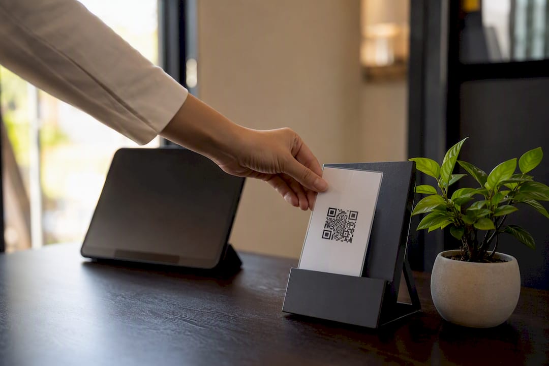 Mano colocando una tarjeta laminada con código QR en un expositor de folletos
