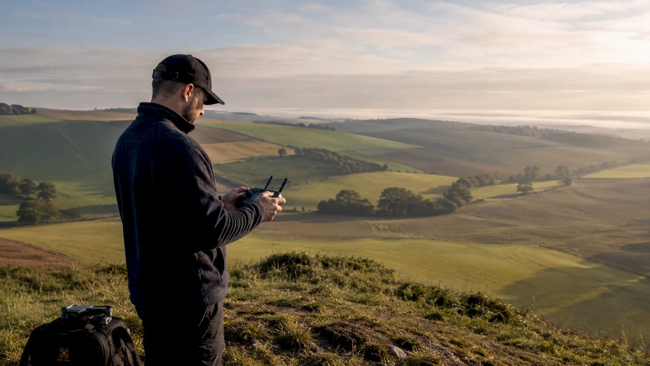 Des mains pilotant un drone qui survole un paysage naturel