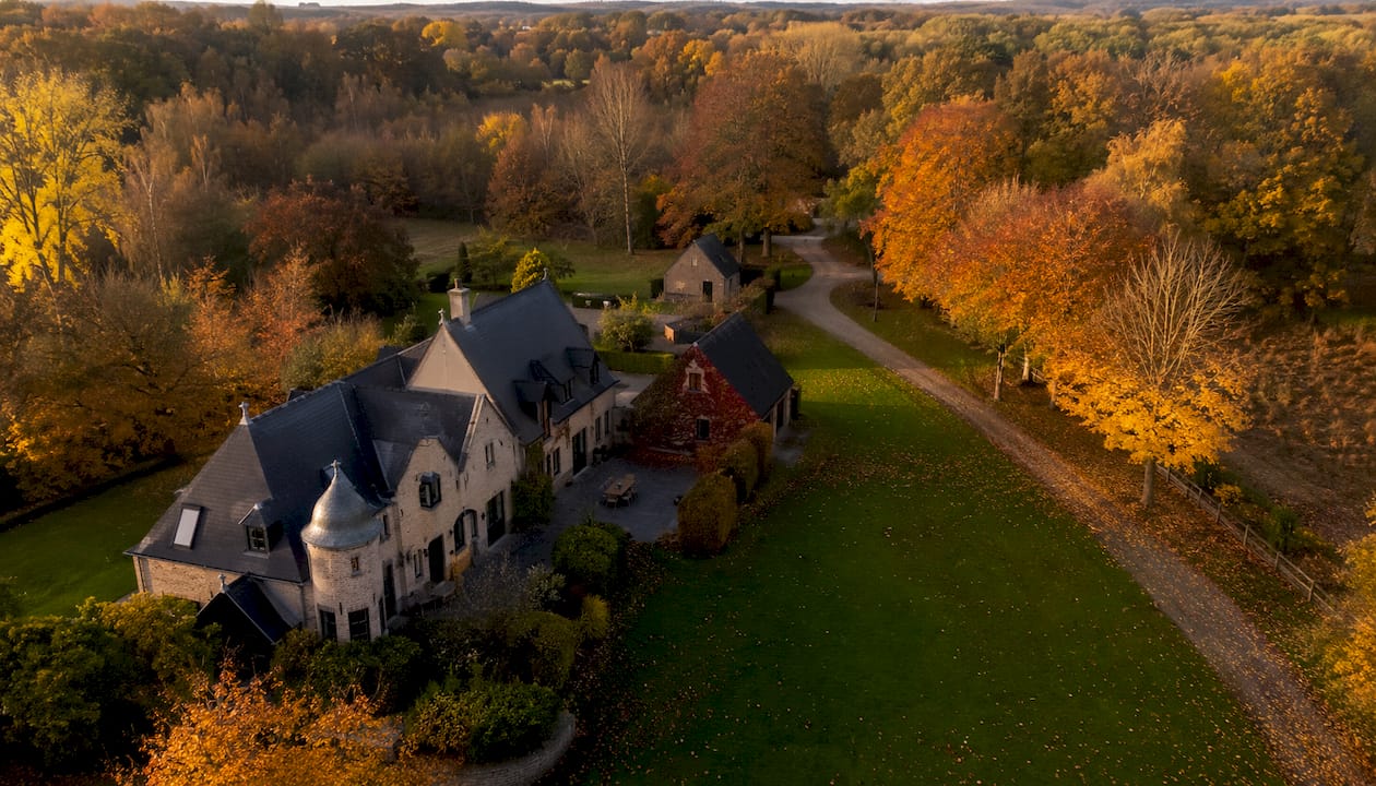 Vue aérienne d’une maison entourée par les couleurs de l’automne, prise par un drone.