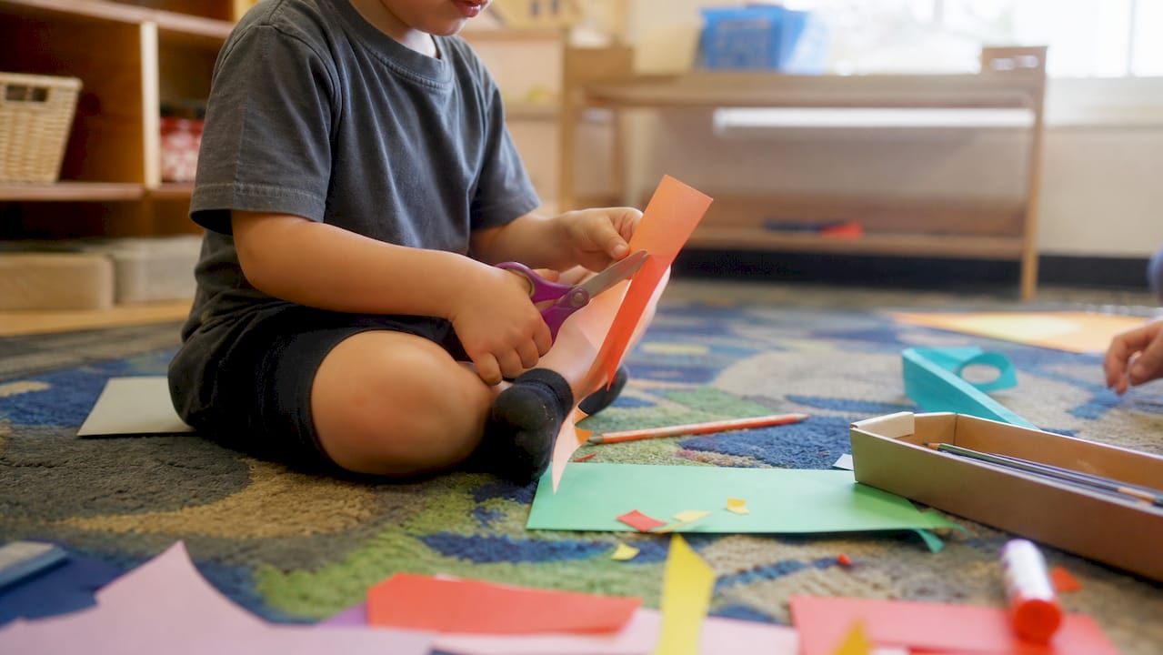 Child practicing cutting skills supervised in classroom