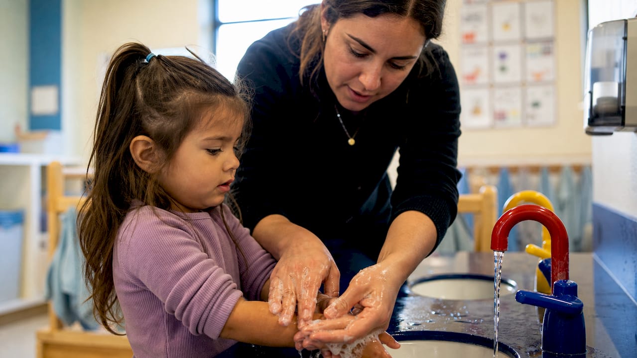 Teacher washing child hands in preschool sink