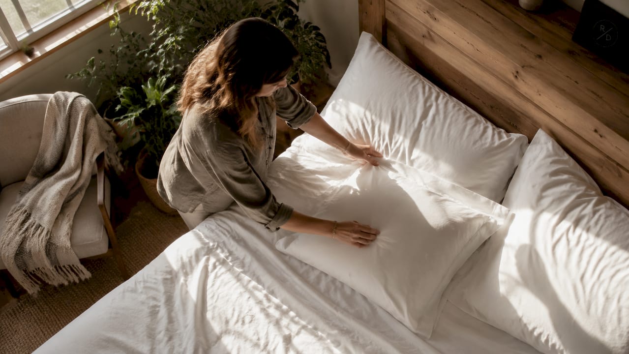 Hands smoothing cotton percale pillowcases on bed