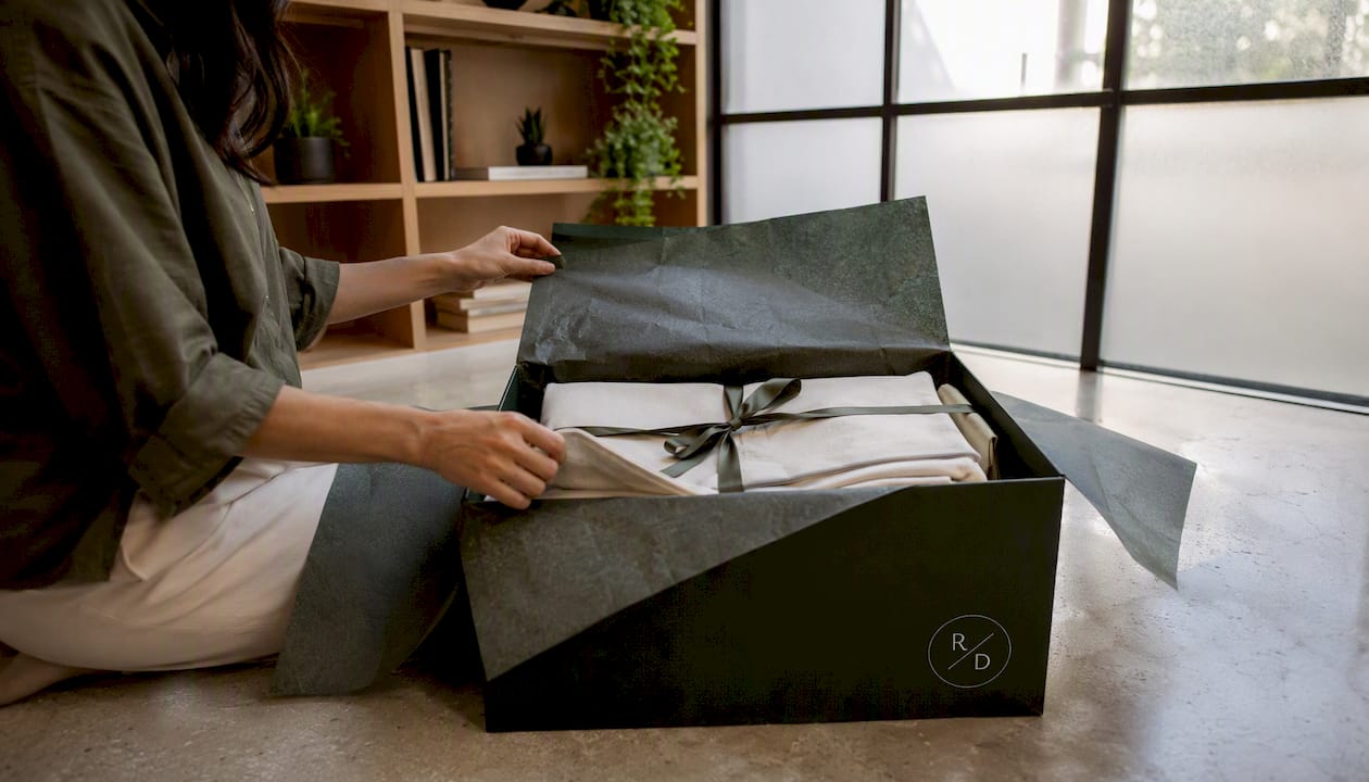 Hands opening luxury bedding package on floor