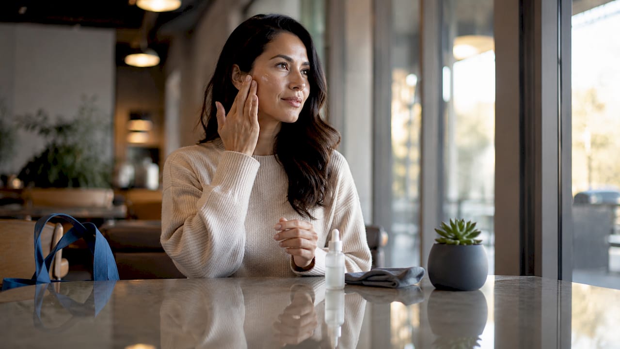 Woman applying serum to face in bathroom