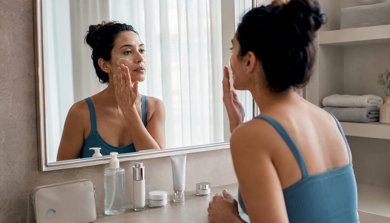 Woman applying sunscreen in bathroom mirror