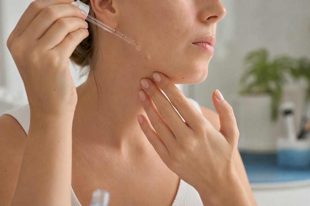 Hands applying serum dropper on cheek skin