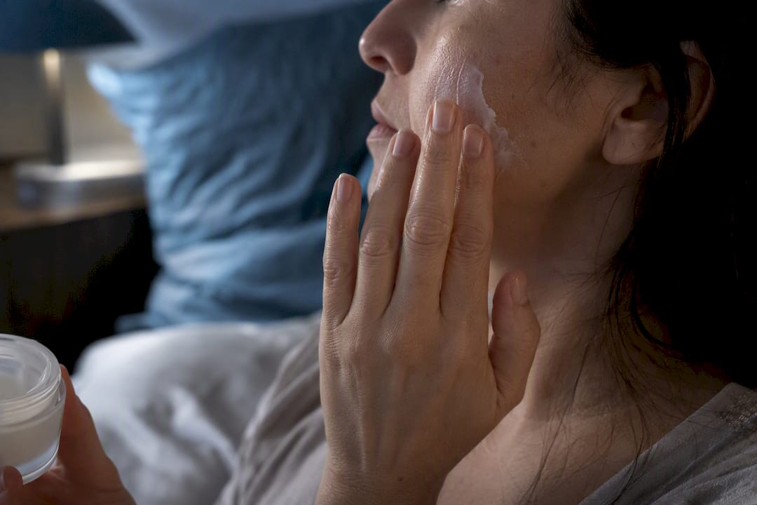 Close-up hands applying rich moisturizer on dry cheek patch