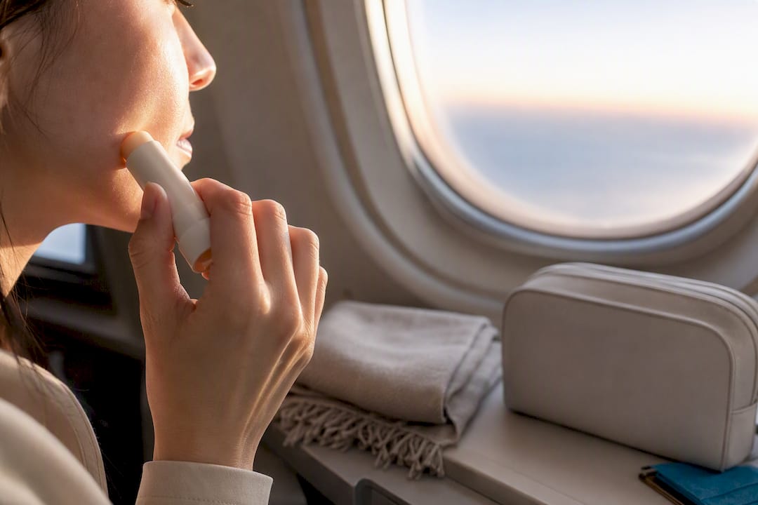 Traveler reapplying balm beside airplane window