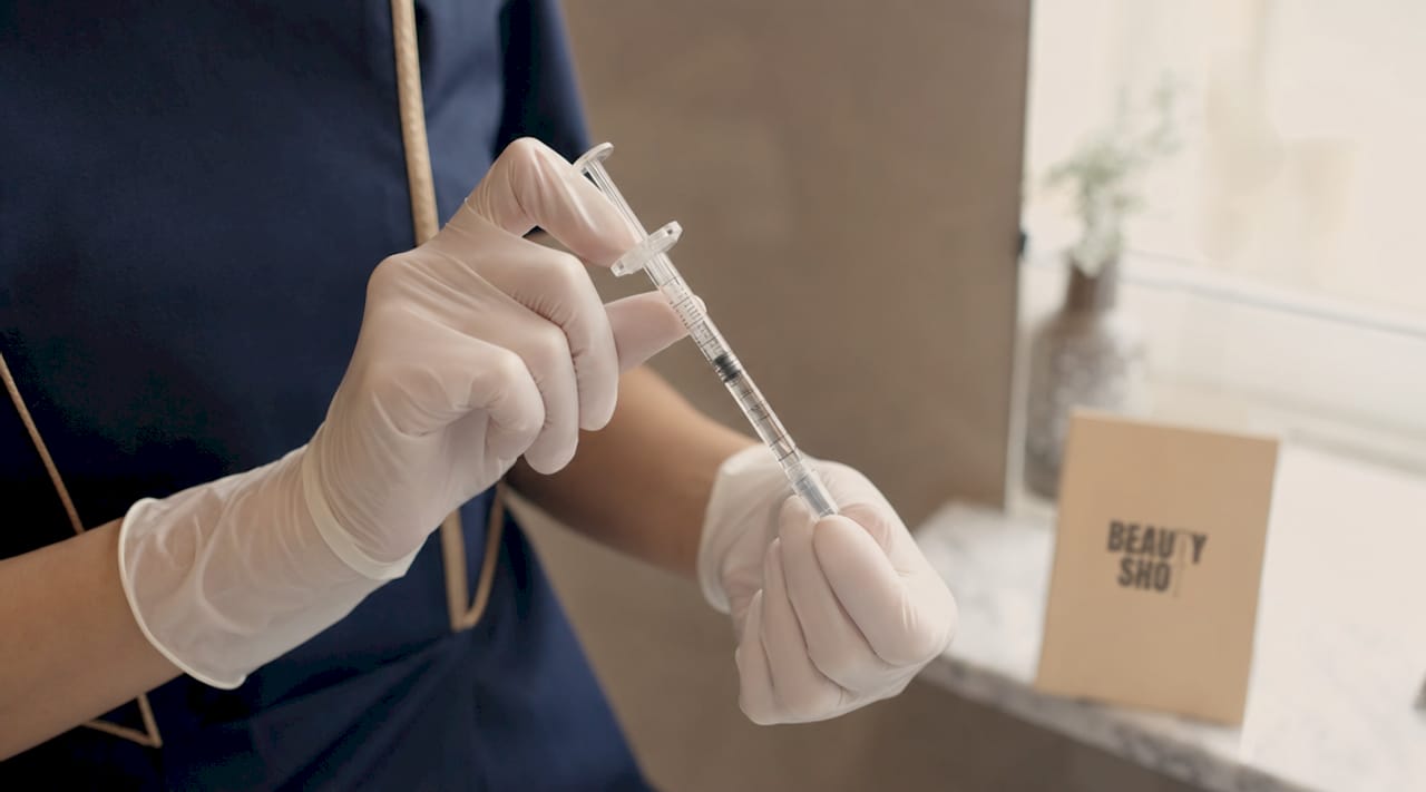 Hands holding dermal filler syringe in clinic