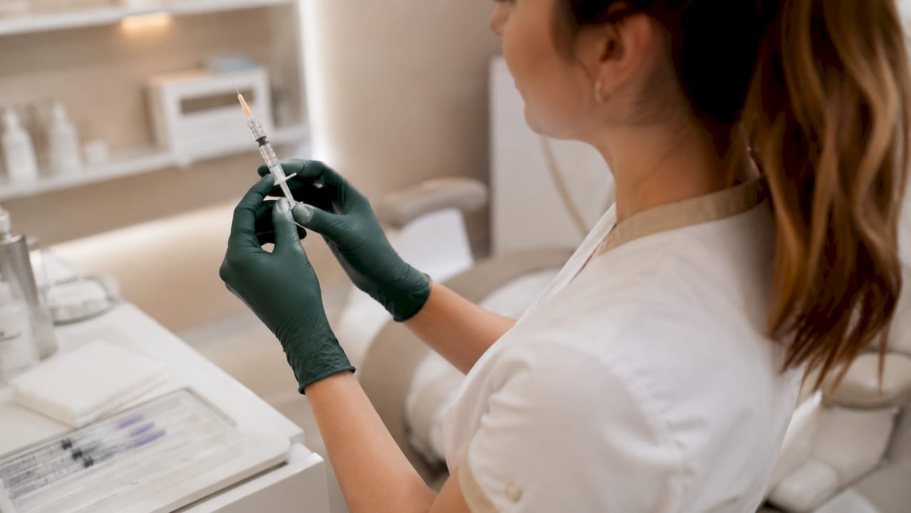 Hands holding syringe with lip filler in clinic