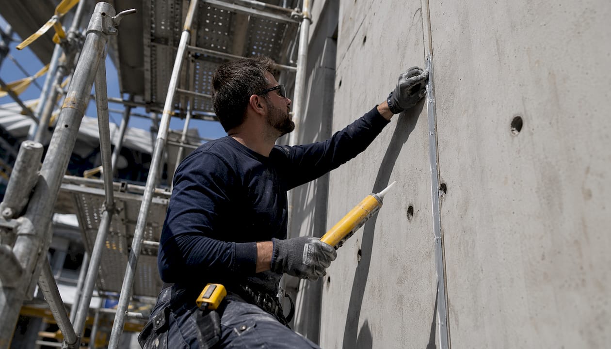 Worker applying caulking to concrete panels