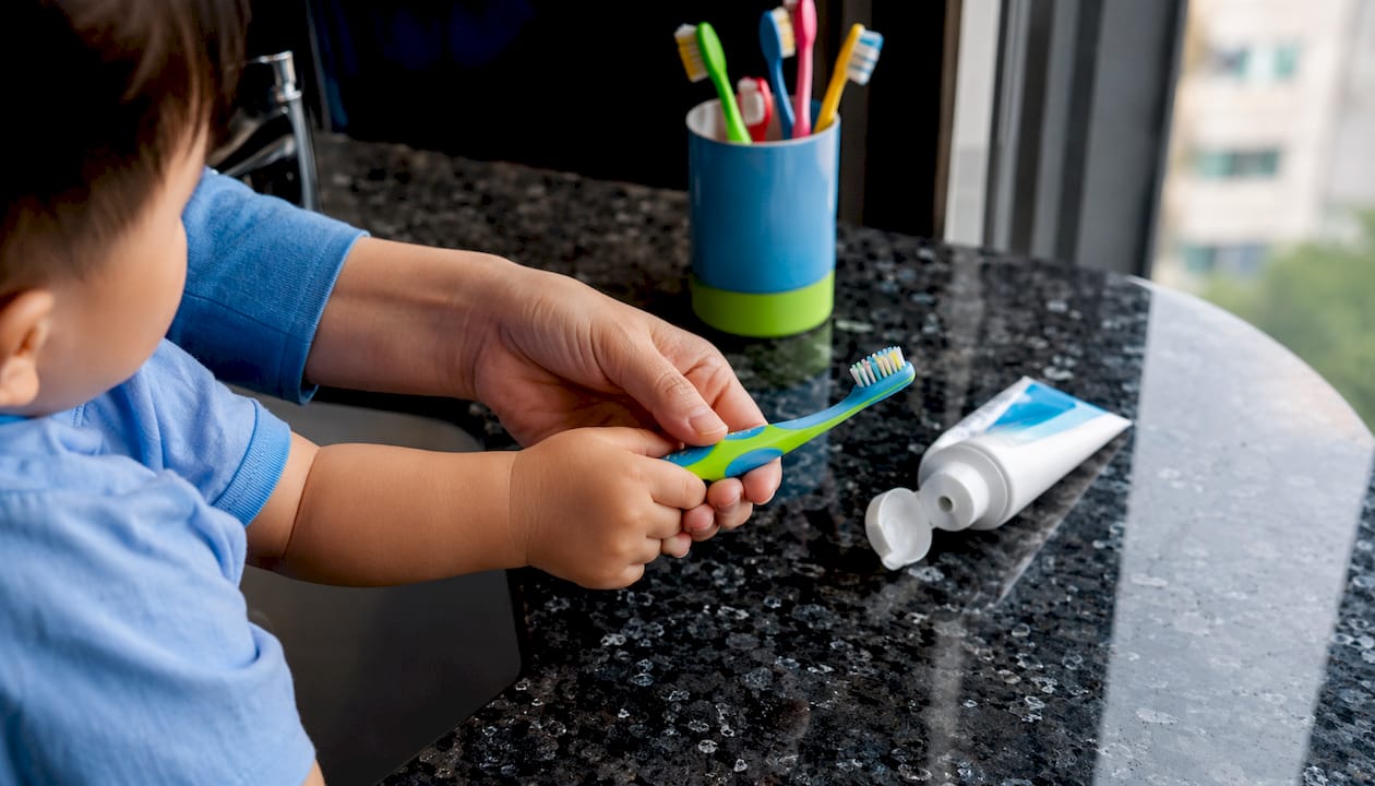 Hands guiding child brushing teeth