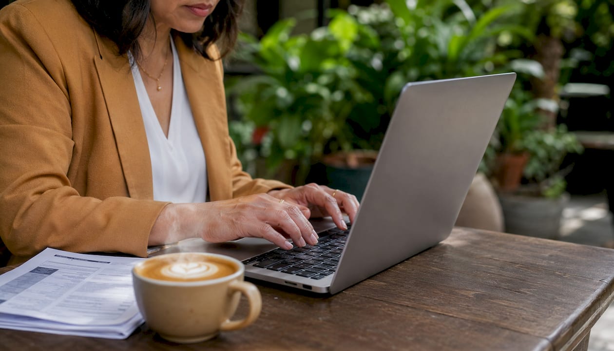 Hands typing beside credit evaluation documents in café