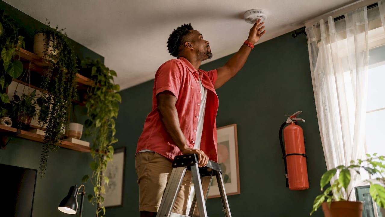 Man testing smoke alarm on ladder indoors