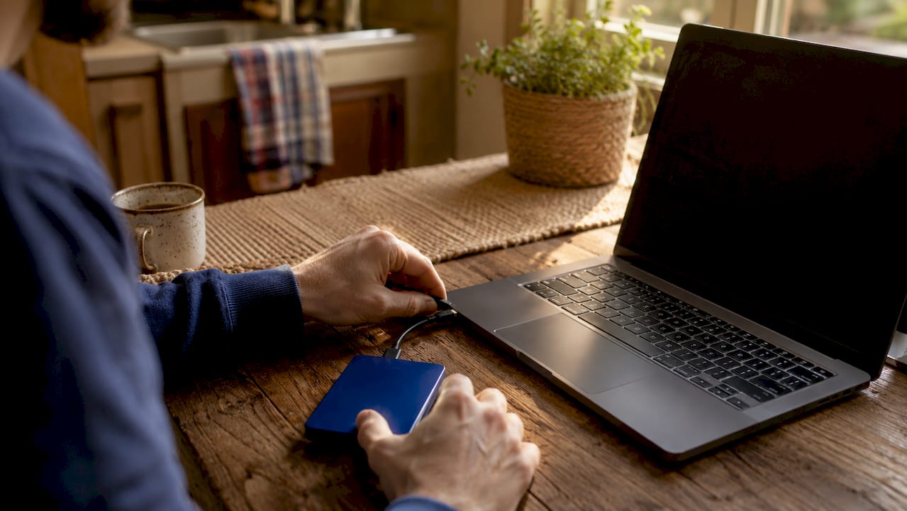 Hands connecting external SSD to laptop for backup