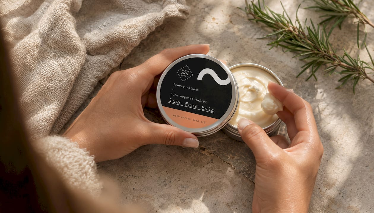Hands scooping whipped body balm from jar on wood table