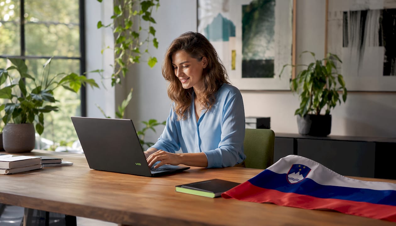 Spletni oblikovalec ustvarja na prenosniku, obdan s slovenskimi motivi.