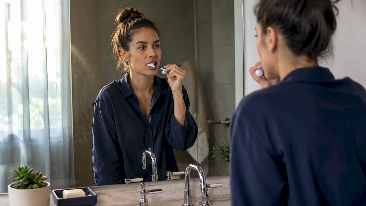 Una persona che si lava i denti davanti allo specchio in bagno.