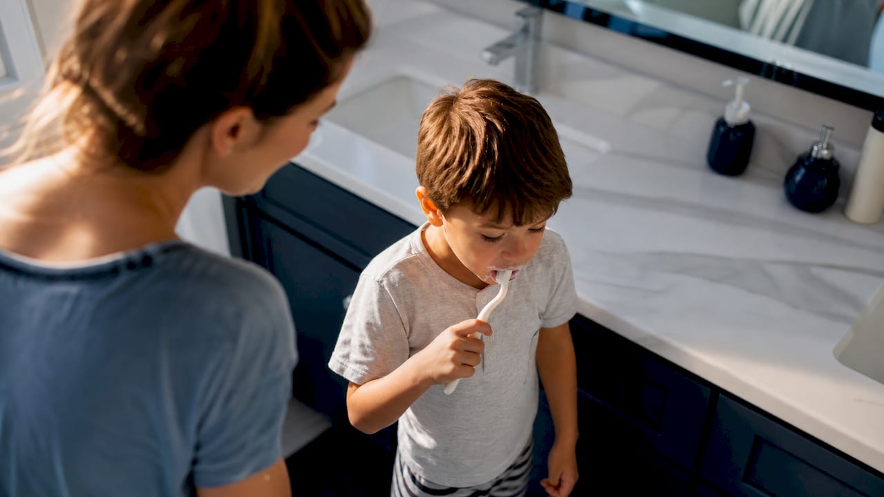 Il bambino si lava i denti mentre un adulto lo osserva per assicurarsi che lo faccia correttamente.