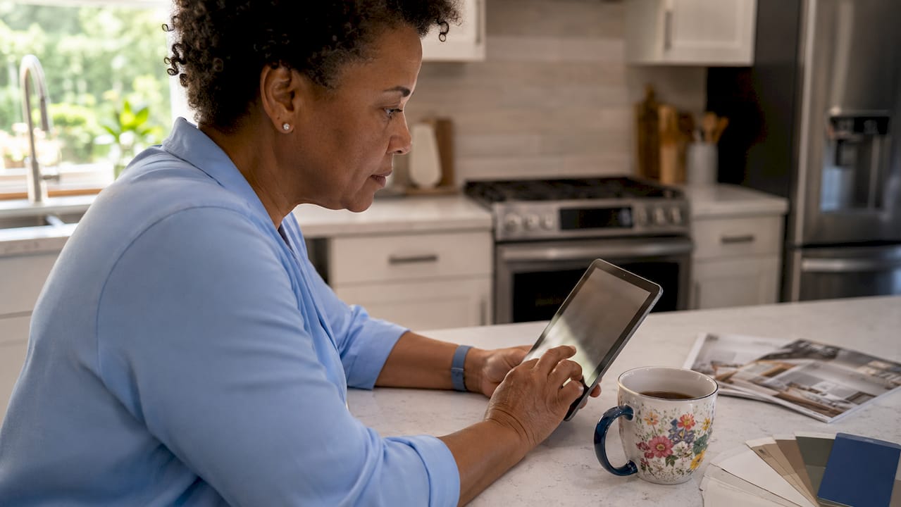 Woman using tablet to track renovation budget at kitchen table