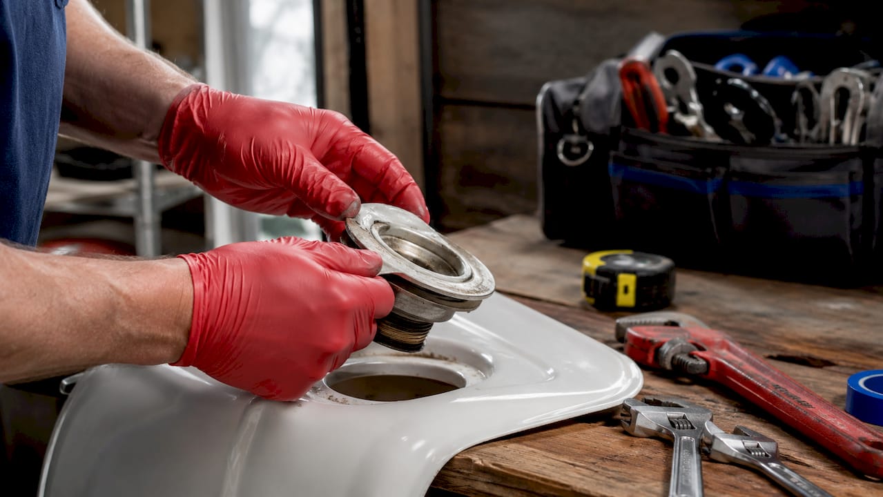Gloved hands removing sink flange sealed with plumber's putty