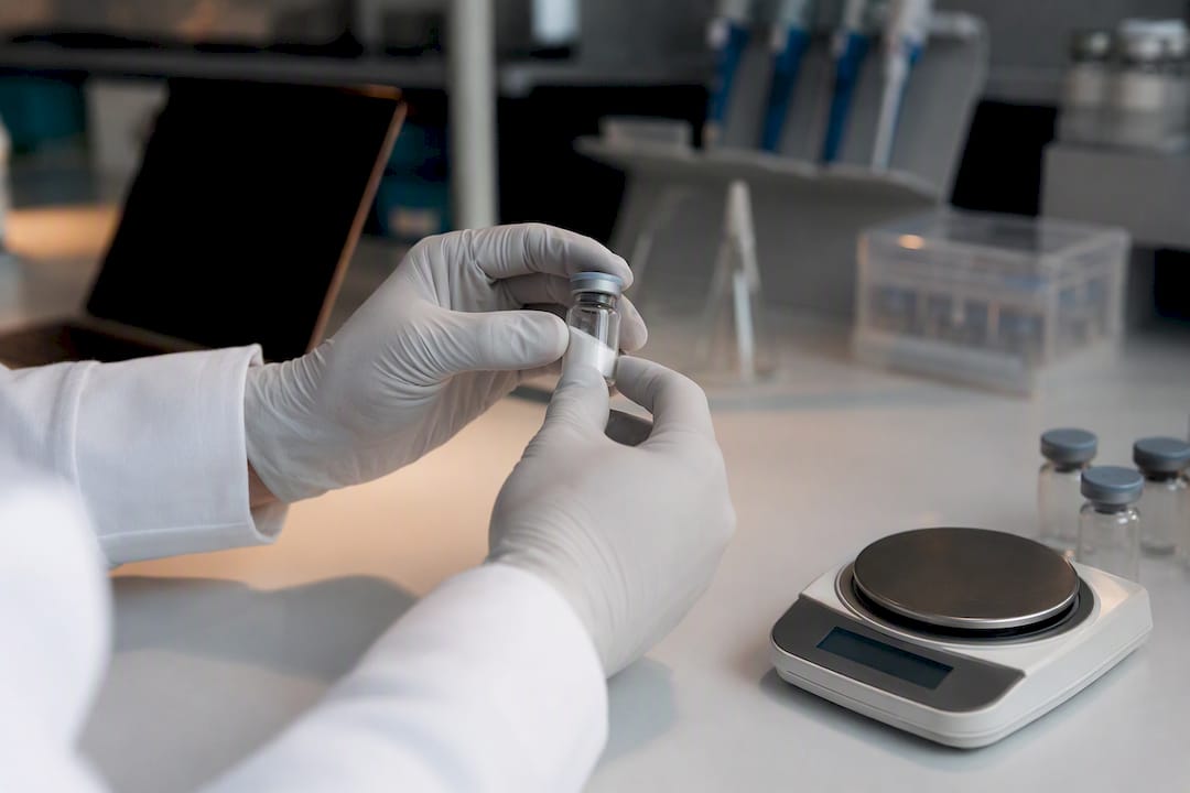 Gloved hands handling peptide vial in lab