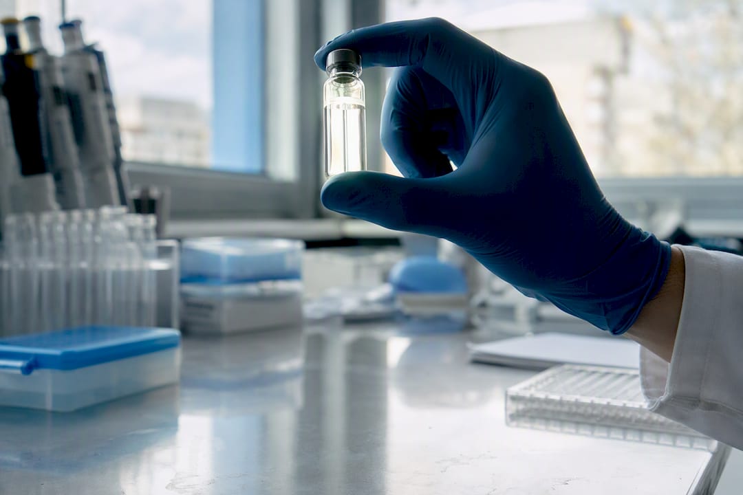 Gloved hand holding peptide vial on lab bench
