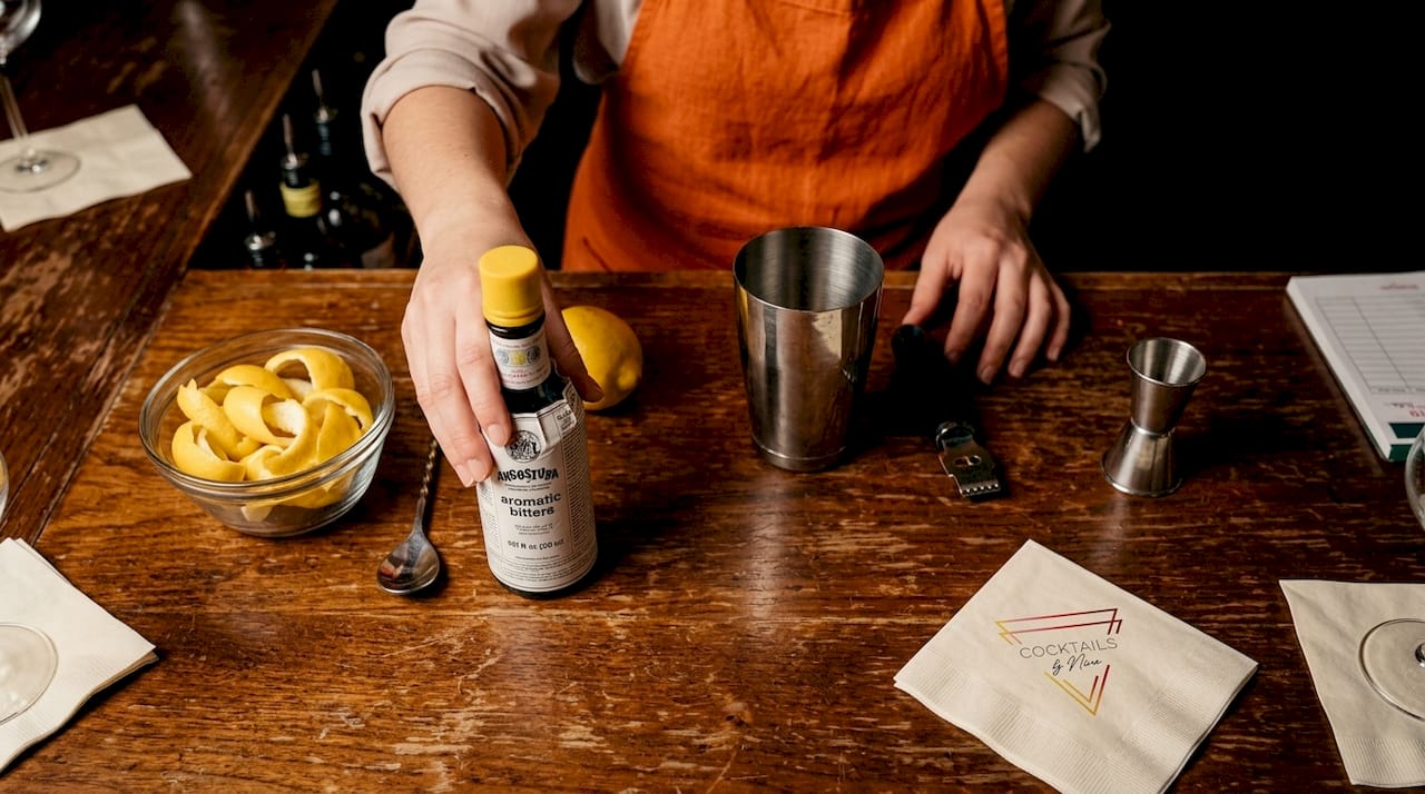 Achter de bar pakt de barman het flesje Angostura bitters om een cocktail te bereiden.