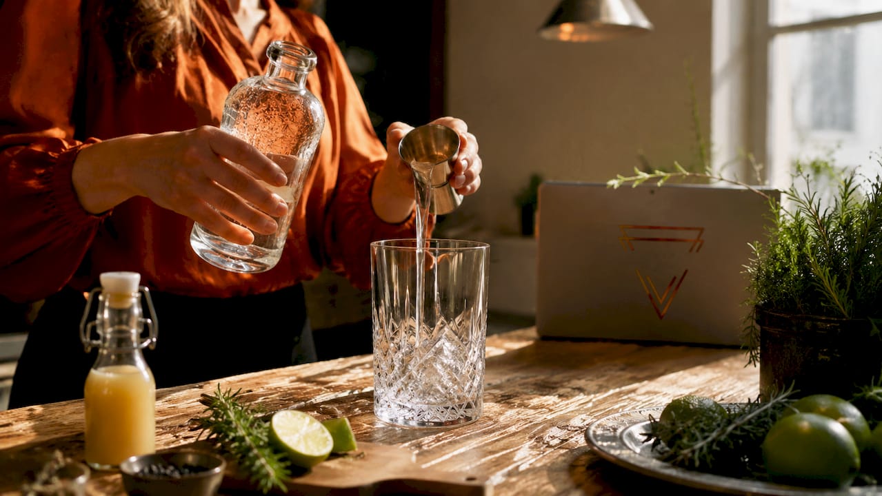 Een paar handen schenken zorgvuldig ambachtelijke gin in een mixglas, klaar om een bijzondere cocktail te maken.