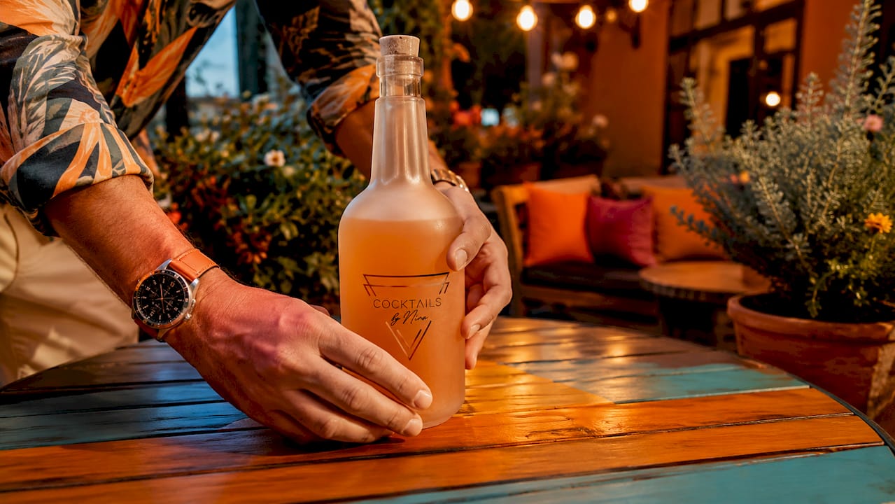 A pair of hands places a stylish cocktail bottle on a beautiful coffee table in the living room.