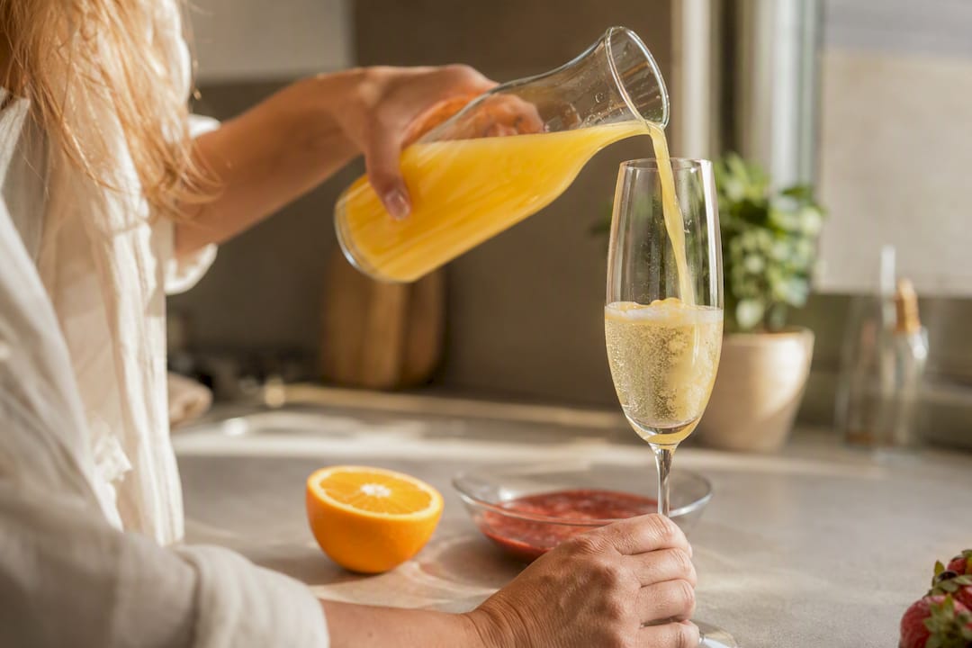 Hands pouring orange juice into a mimosa glass