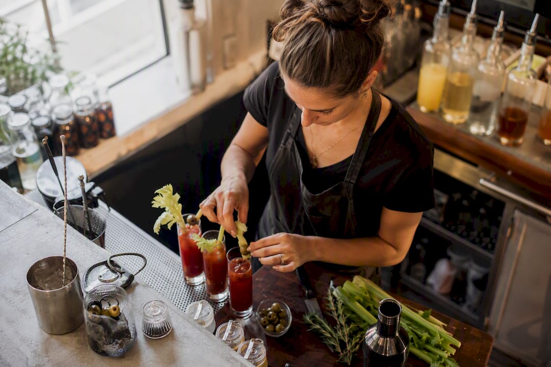 Hands stirring a Bloody Mary cocktail with garnishes