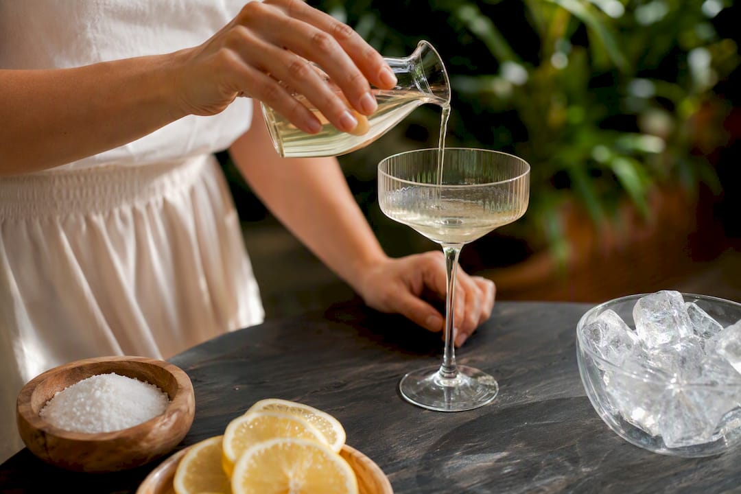 Handen die zoetstof in een cocktailglas schenken vóór het ijs