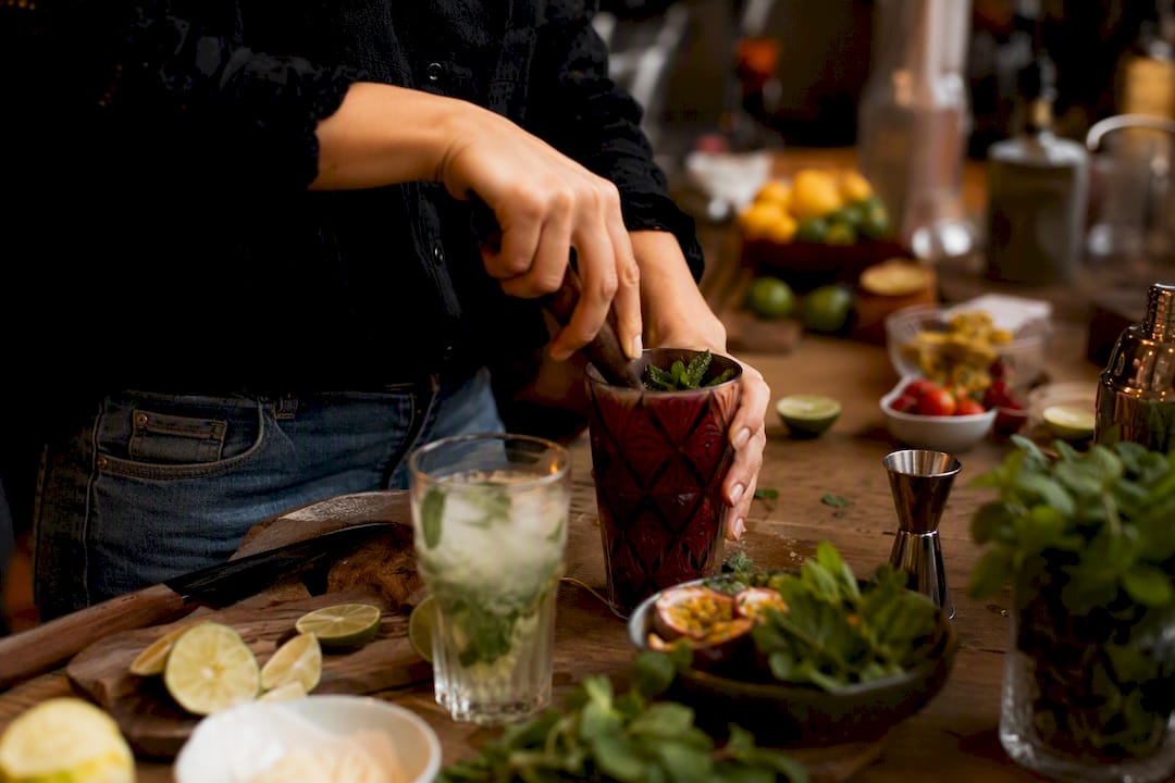 Handen die kruiden stampen tijdens cocktailworkshop