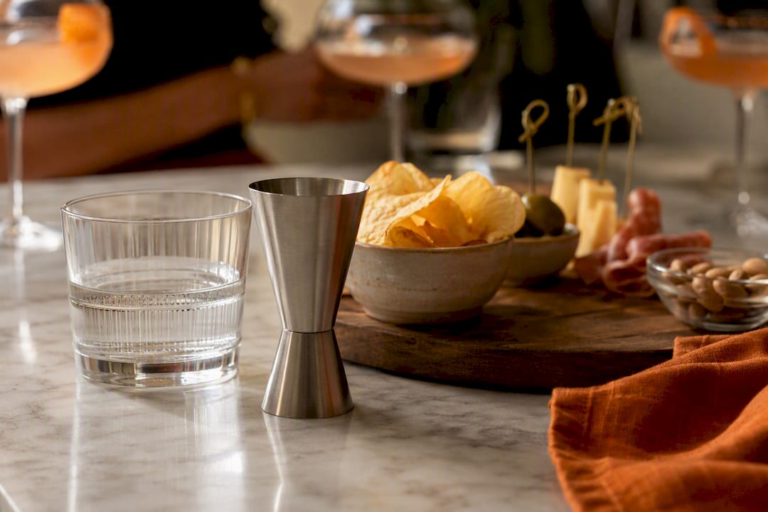 Jigger gevuld met water en hapjes naast cocktails